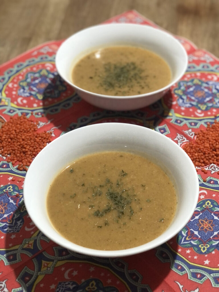 Two bowls of Turkish lentil soup, served on festive napkins with traditional Arab patterns, famous for Ramadan festivities. There is raw lentil next to the bowls for decoration.