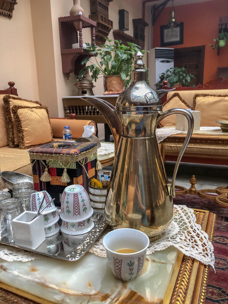 a tall arabic coffee pot with small ceramic cups with oriental sofas in the background
- Among only ladies again